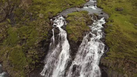 Aerial-rising-over-Glymur-waterfalls-and-river-streaming-down-rocky-cliff-surrounded-by-verdant-highlands-at-daytime,-Iceland