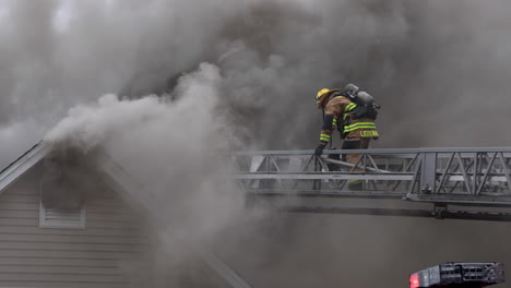 Zwei-Feuerwehrleute-Laufen-über-Eine-Ausziehbare-Leiter-Auf-Dichten,-Dunklen-Rauch-Zu,-Der-Aus-Einem-Brennenden-Haus-Austritt