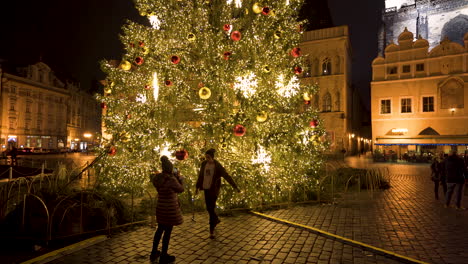 Girl-taking-pictures-of-boyfriend-with-Prague-Christmas-tree,evening