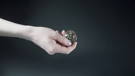 Hand-holding-shiny-Bitcoin-cryptocurrency-coin,-black-background