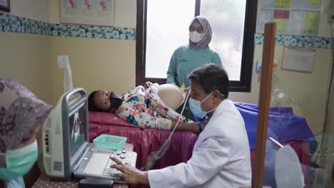 Side-view-of-Indonesian-male-doctor-performing-ultrasound-scan-for-pregnant-woman-in-hospital,-accompanied-by-a-midwife