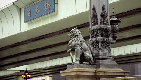 TOKYO,-JAPAN,-circa-April-2020:-pedestrians-walking-on-historical-Nihonbashi-bridge-with-carved-lion-sitting,-highway-overhead,-at-old-downtown-in-central-financial-area,-spring-evening