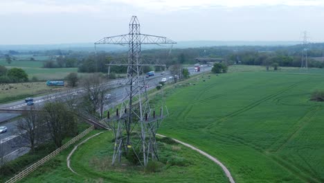 Vehicles-on-M62-motorway-passing-pylon-tower-on-countryside-farmland-fields-aerial-view-ascending