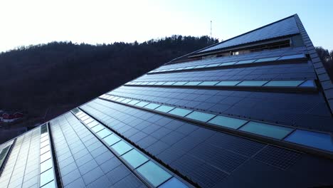 Solar-panels-on-roof-of-office-building-Powerhouse-in-Porsgrunn-Telemark-Norway---Slow-evening-aerial-showing-rooftop-of-modern-building-producing-more-electricity-than-it-consumes