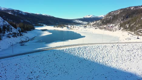Slow-aerial-view-of-Statkraft-operatedTunhovd-dam-with-Tunhovdfjord-water-reservoir-inside---Low-fill-grade-during-sunny-winter-day---Road-crossing-on-top-with-blue-sky-background-in-Nore-and-Uvdal
