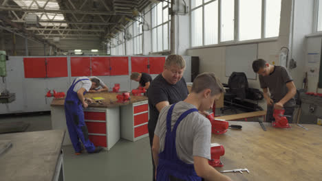 Trainees-Under-Teacher's-Supervision-Sanding-Edge-Of-A-Steel-Plate-In-Metal-Vise-Grip-On-Working-Table