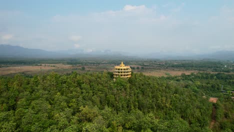 Aerial-drone-flying-low-over-a-dense-forest-towards-a-golden-Wat-Doi-Sapanyoo-in-the-mountain-hills-of-Chiang-Mai-Thailand-on-a-sunny-summer-day