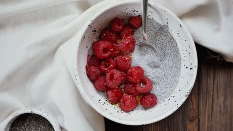 Close-Up-Shot-of-a-White-Bowl-filled-with-Raspberries-and-Chia-Seeds-on-a-wooden-table