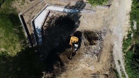 Yellow-crave-aerial-top-down-view-of-excavator-truck-working-in-remote-area-construction-site-for-build-residential-district-in-natural-environment