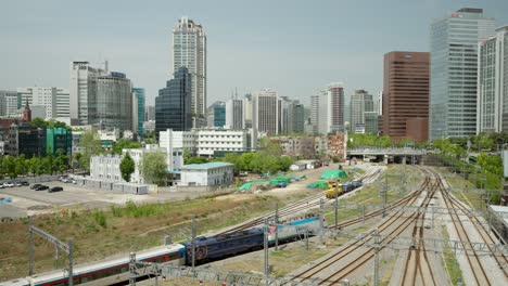 Korail-Passenger-Train-Departing-from-Seoul-Station-Depot-with-City-Skyline-in-Background,-South-Korea
