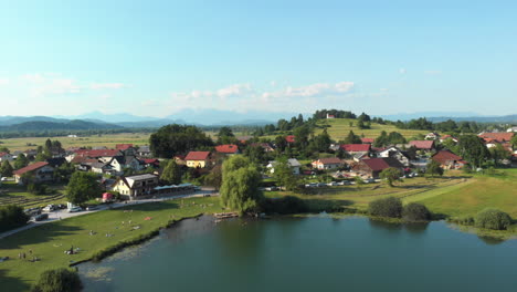 Aerial-view-flying-up-over-the-lake-of-Podpeč-and-the-village-of-Jezero-in-Slovenia-with-blue-sky-and-clouds-and-beautiful-view-of-the-surroundings