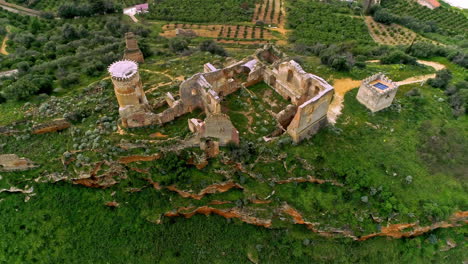 Aerial-drone-backward-moving-shot-of-ruins-of-an-old-building-on-the-hill-top-with-a-winding-river-flowing-in-the-background-in-north-of-Troina,-Sicily,-Italy-withgreen-vegetation-on-a-cloudy-day