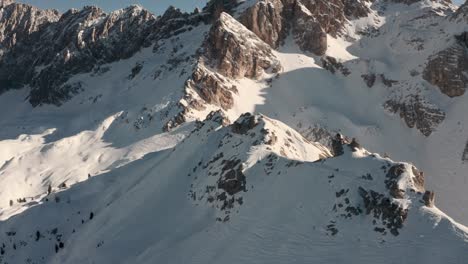 Dolly-forward-pan-up-drone-shot-along-snowy-mountain-ridge-towards-large-rock-falls