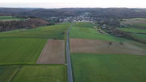 A-long-country-road-leading-through-differently-coloured-fields-and-meadows-in-Hesse,-Germany-at-sunset