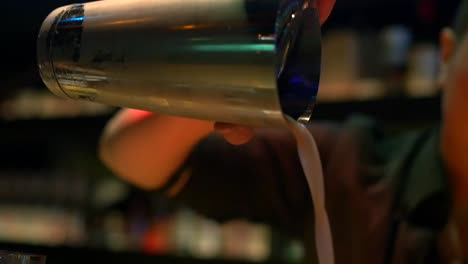 Asian-bartender-using-stainless-steel-cocktail-shaking-cup-to-pour-freshly-mixed-tropical-cocktail-into-glass-filmed-as-close-up-in-slow-motion