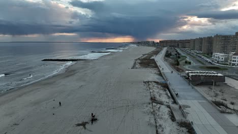 An-aerial-view-of-a-quiet-beach-in-Arverne,-NY-as-rain-falls-in-the-distance-on-a-cloudy-evening