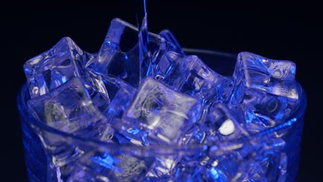 Static-shot-of-artistic-cocktail-with-blue-light-and-coloring-being-poured-over-ice-with-a-black-background,-no-garnish,-on-the-rocks