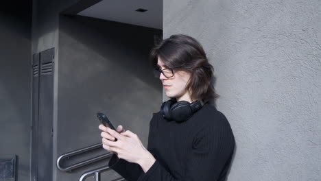Junger-Mann-Mit-Brille,-Kopfhörer-Um-Den-Hals,-SMS-Auf-Seinem-Handy-Schreibend