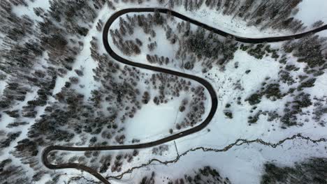 Drone-zenith-Aerial-view-of-narrow-street-in-the-mountains-among-the-forest-with-snow-in-winter