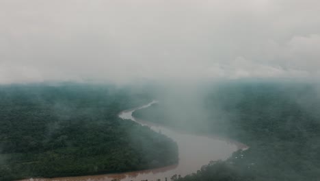 Drone-flight-between-clouds-over-dense-jungle-of-Peru-with-brown-colored-Amazon-River