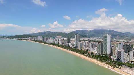 wide-aerial-drone-of-Nha-Trang-on-a-sunny-summer-day-with-camera-moving-towards-the-coastline-and-white-sand-beach-as-traffic-drives-past-the-tall-skyscraper-residential-buildings