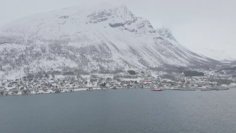 Kåfjord-town-centre-and-harbour-at-the-foot-of-a-snowy-mountain-in-Olderdalen,-Norway