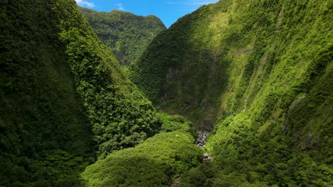 Aerial-view-of-a-ravine-on-the-Reunion-Island,-sunlight-break-through-the-clouds,-the-mountain-is-covered-in-green-vegetation