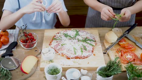 Still-shot-of-two-cooks-setting-toppings-on-a-homemade-pizza-placed-on-a-wooden-cutting-board