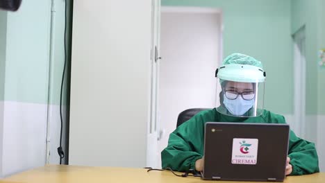 Young-Asia-lady-doctor-in-blue-medical-uniform-with-hijab-using-computer-laptop-talking-video-conference-call-with-patient-at-desk-in-health-clinic-or-hospital