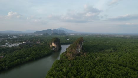 Aerial-drone-panning-right-over-a-mangrove-forest-and-river-running-between-two-large-limestone-mountain-rocks-on-a-sunset-afternoon-in-Krabi-Town-Thailand