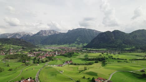 Flying-over-a-bavarian-village-in-the-alps-with-mountains-in-the-background