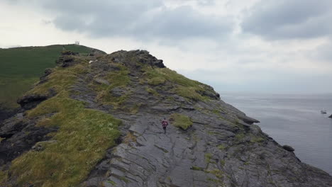 Aerial-camera-follows-man-as-he-runs-up-rugged-rocky-outcrop-in-UK