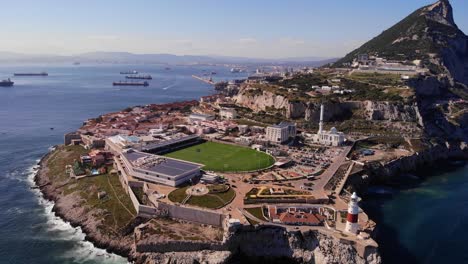 Grünes-Stadion-Der-Rugby-Union-Nationalmannschaft-Von-Gibraltar-Am-Europa-Point-Mit-Dem-Erkennbaren-Leuchtturm-über-Den-Hohen-Klippen-Und-Felsen,-Wo-An-Einem-Sonnigen-Tag-Die-Wellen-Brechen