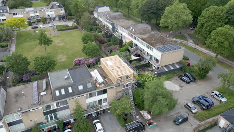 Aerial-overview-of-wooden-frame-of-roof-structure-under-construction-in-a-busy-suburban-neighborhood---Drone-flying-backwards