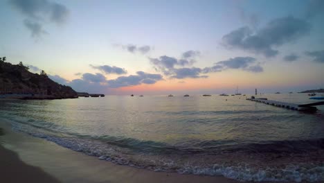 Wide-view-of-Konnos-Bay-at-sunset-as-waves-wash-ashore-with-boats-anchored-in-the-water