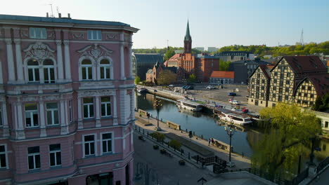 Aerial-view-of-docking-boats-on-Brda-River-and-Saint-Andrew-Bobola's-Church-during-sunny-day