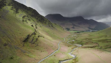 A-car-in-the-distance-drives-through-a-vast-valley-in-the-English-Lake-District,-moody-clouds-overhead-on-an-overcast-day