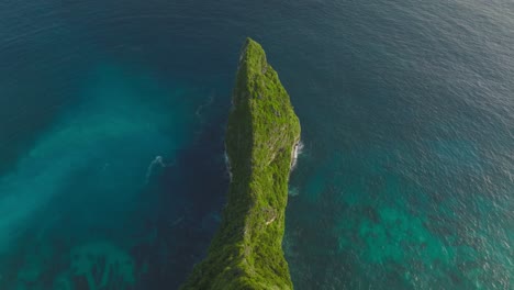 Lush-green-Sekartaji-cliff-surrounded-by-turquoise-and-blue-sea-water,-aerial