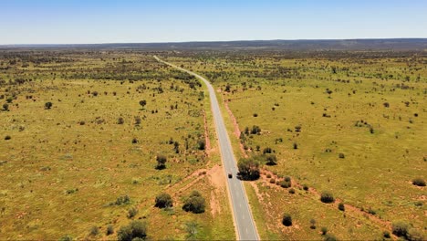 Long-drone-shot-of-a-car-driving-into-the-distance-of-a-never-ending-road-in-the-country