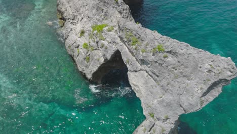 Cinematic-shot-of-famous-rock-arch-on-Nusa-Batupadasan-at-Atuh-Beach,-aerial