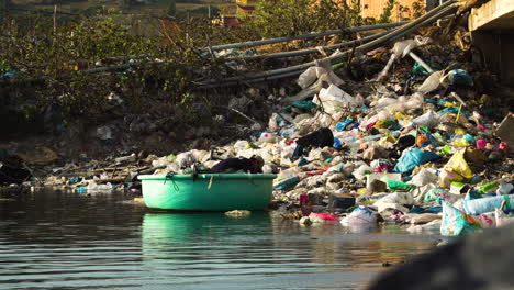 Mann-In-Rundem-Vietnamesischem-Boot-Inspiziert-Flussufer,-Das-Mit-Plastikmüll-Verschmutzt-Ist