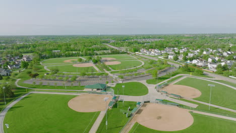 Flying-Over-Baseball-Diamonds,-Aerial-Drone-Shot-of-Bright-Green-Baseball-Fields-on-Sunny-Day