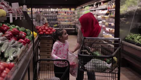 Little-girl-helping-mother-at-the-grocery-store,-putting-vegetables-in-a-bag