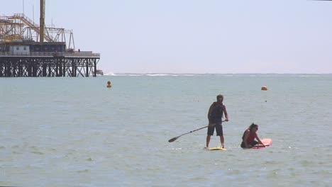 Brighton,-England---August-11-2018:-A-sporting-couple-using-paddle-boards-as-recreation-on-a-sunny-day-in-front-of-the-skeletal-burnt-out-remains-of-the-main-Pier-in-Brighton