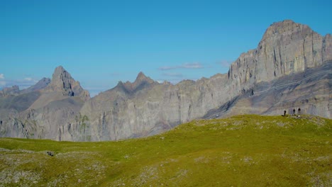 Aerial-reveal-and-orbit-around-hikers,-Grand-Muveran-massif-and-the-Alps-in-the-background,-Switzerland-Shot-using-long-lens-to-accentuate-background-compression-Col-des-Perris-Blancs