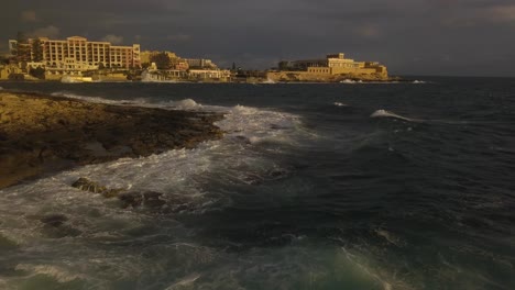 Low-altitude-aerial-view-flying-forward-over-rolling-waves-as-they-crash-on-the-rocky-shoreline-of-Malta
