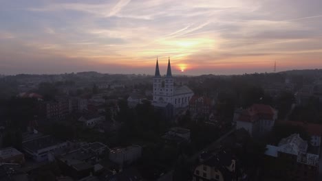 Aerial-shot-of-a-christian-church-in-small-european-town-during-foggy-sunrise
