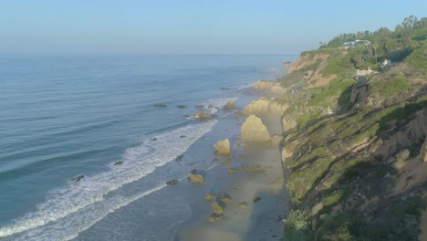 Aerial-shots-of-El-Matador-beach-over-breaking-waves-and-rocks-on-a-hazy-summer-morning-in-Malibu,-California