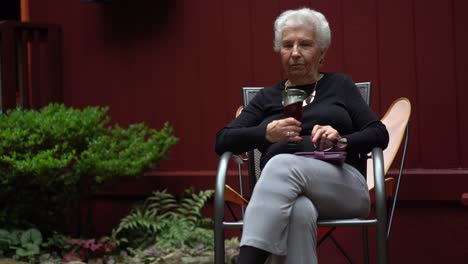 Ältere-Frau-Lächelt-Und-Sitzt-Draußen-In-Einem-Garten,-Während-Sie-Rotwein-Trinkt