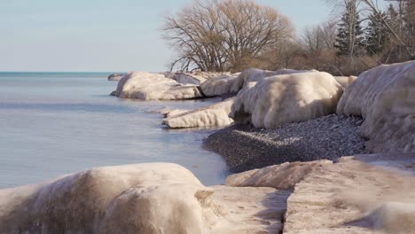 a-winter-pebble-beach-with-small-waves-flowing-and-large-melting-ice-chunks-in-4k